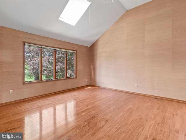 unfurnished room featuring lofted ceiling, light wood-style floors, a skylight, and baseboards