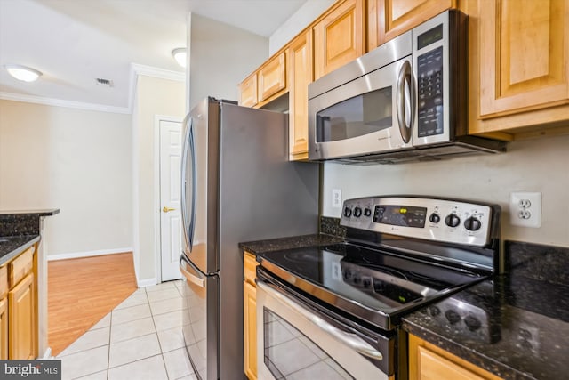 kitchen featuring appliances with stainless steel finishes, ornamental molding, light brown cabinets, light tile patterned floors, and dark stone counters
