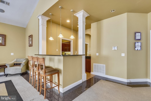 kitchen with baseboards, decorative columns, a kitchen bar, and decorative light fixtures
