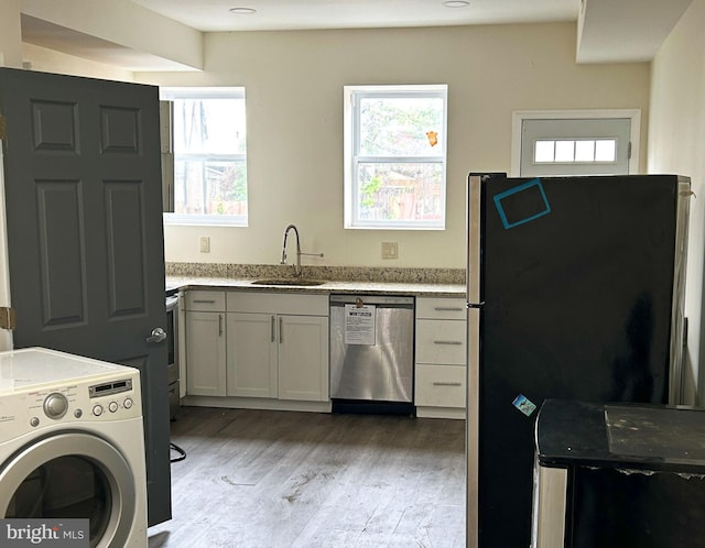 kitchen featuring stainless steel appliances, washer / dryer, a sink, light wood-type flooring, and healthy amount of natural light