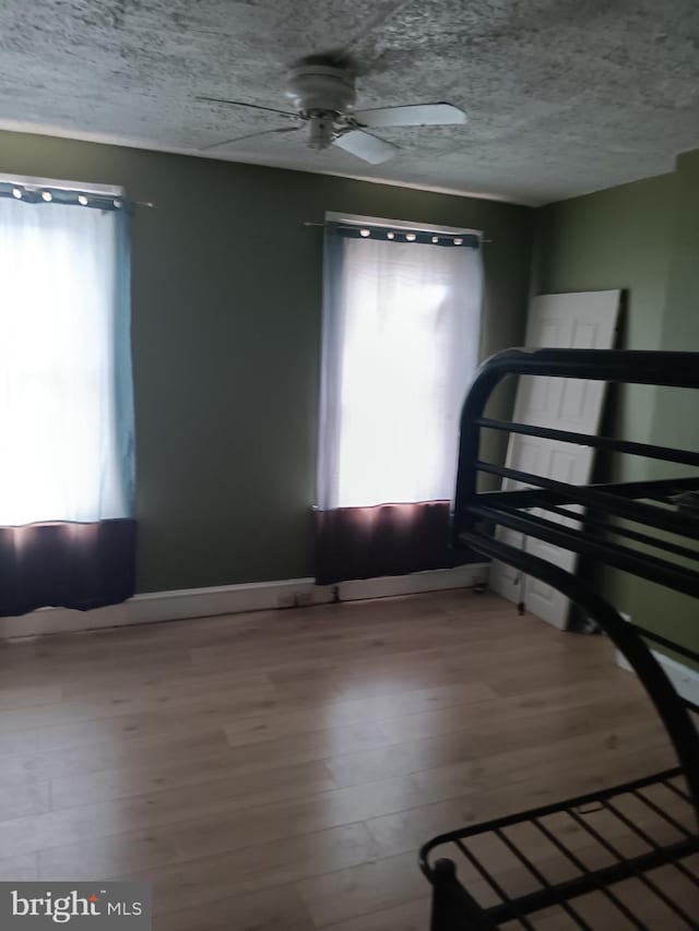 unfurnished bedroom featuring multiple windows, wood finished floors, baseboards, ceiling fan, and a textured ceiling