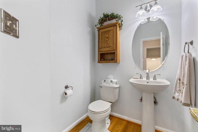 half bathroom featuring wood finished floors, baseboards, and toilet