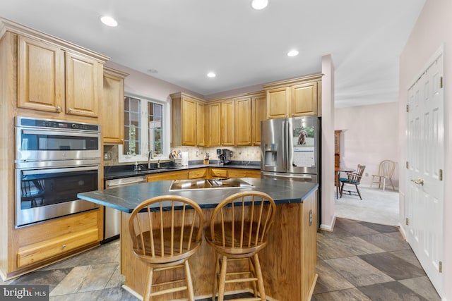 kitchen featuring appliances with stainless steel finishes, dark countertops, a sink, a breakfast bar, and recessed lighting