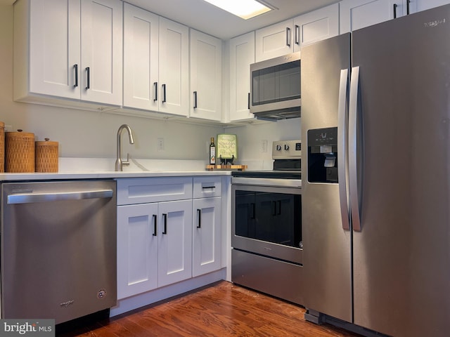 kitchen with stainless steel appliances, a sink, dark wood-style floors, white cabinetry, and light countertops