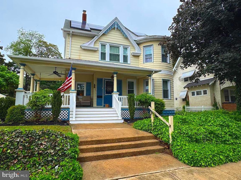 victorian home featuring a porch, ceiling fan, solar panels, and a chimney