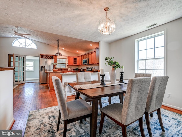 dining space featuring a textured ceiling, hardwood / wood-style flooring, a chandelier, vaulted ceiling, and baseboards