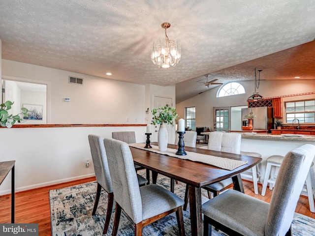 dining area with a textured ceiling, light wood-type flooring, a chandelier, lofted ceiling, and baseboards