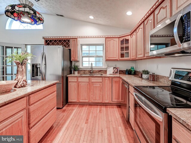 kitchen featuring stainless steel appliances, vaulted ceiling, a sink, light wood finished floors, and light stone countertops