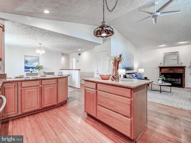 kitchen with a textured ceiling, open floor plan, a glass covered fireplace, vaulted ceiling, and light wood-style flooring