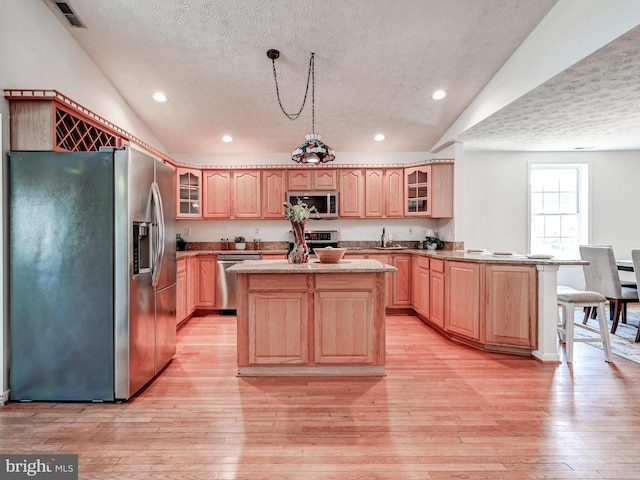 kitchen with appliances with stainless steel finishes, a textured ceiling, vaulted ceiling, a peninsula, and light brown cabinetry