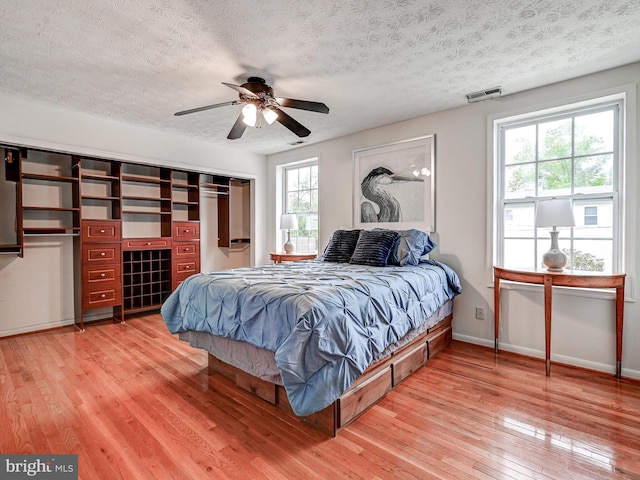bedroom with light wood-style flooring, a textured ceiling, baseboards, and ceiling fan