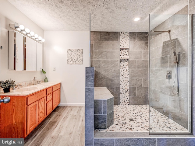 full bathroom with wood finished floors, a textured ceiling, a walk in shower, vanity, and baseboards