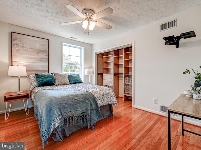 bedroom with baseboards, light wood-type flooring, a textured ceiling, a closet, and ceiling fan