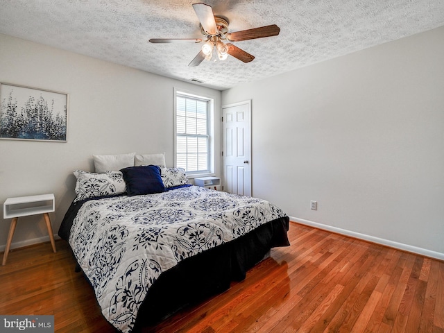 bedroom featuring baseboards, a textured ceiling, wood-type flooring, and ceiling fan