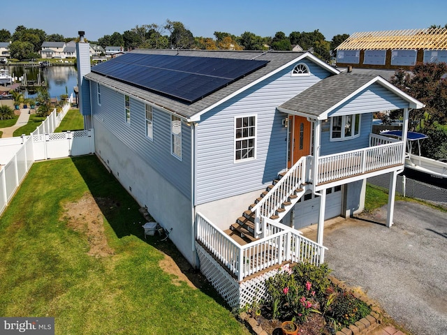 view of front of home with a shingled roof, solar panels, an attached garage, stairway, and a water view