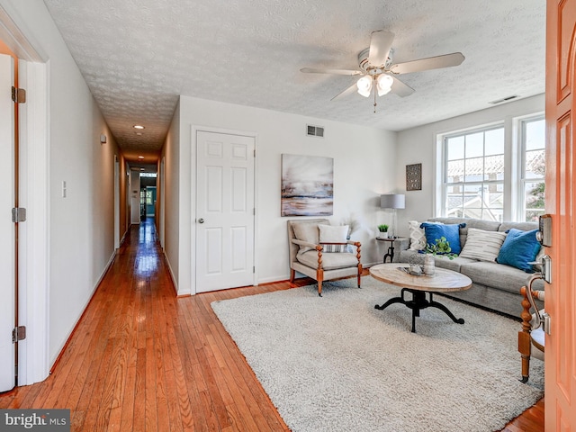 living room featuring a textured ceiling, light wood finished floors, a ceiling fan, and baseboards