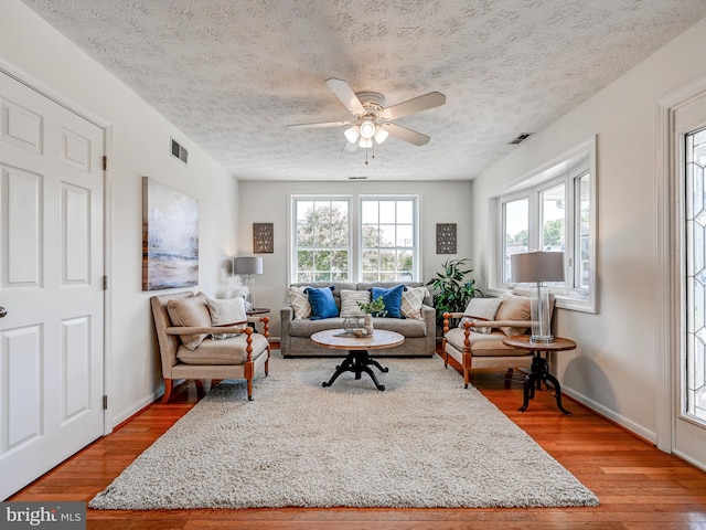living area with light wood-style floors, ceiling fan, a textured ceiling, and baseboards