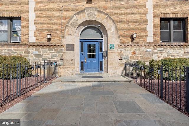 doorway to property featuring brick siding, stone siding, and fence