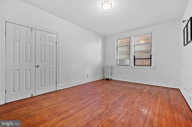 unfurnished bedroom featuring radiator, hardwood / wood-style flooring, baseboards, and cooling unit