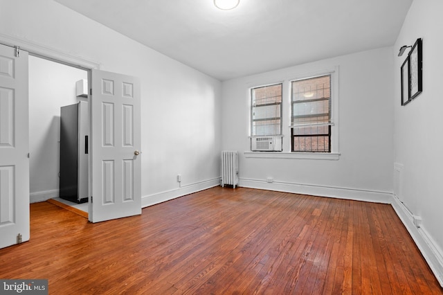 unfurnished bedroom featuring radiator, wood-type flooring, freestanding refrigerator, and baseboards