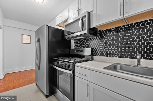 kitchen with stainless steel appliances, a sink, white cabinets, light countertops, and decorative backsplash