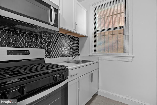 kitchen featuring stainless steel appliances, a sink, backsplash, and white cabinetry