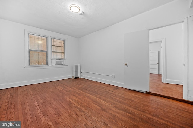 empty room with radiator heating unit, hardwood / wood-style flooring, baseboards, and cooling unit
