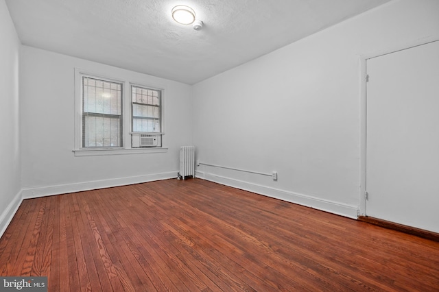 unfurnished room with radiator, dark wood-style floors, baseboards, and cooling unit