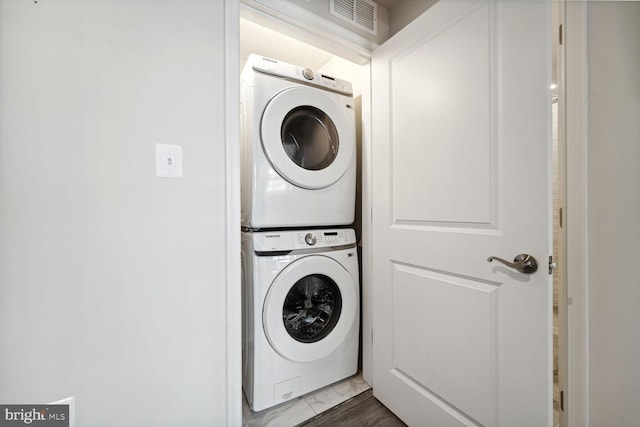clothes washing area with estacked washer and dryer and marble finish floors