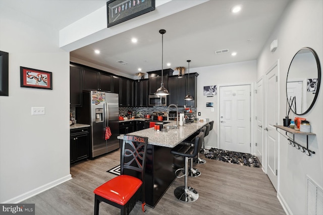 kitchen with appliances with stainless steel finishes, light wood-style floors, backsplash, a kitchen bar, and light stone counters