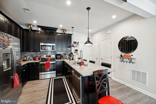 kitchen featuring stainless steel appliances, a sink, light wood finished floors, light stone counters, and recessed lighting