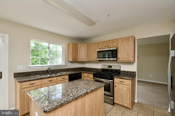 kitchen with appliances with stainless steel finishes, a sink, light brown cabinets, and dark stone counters