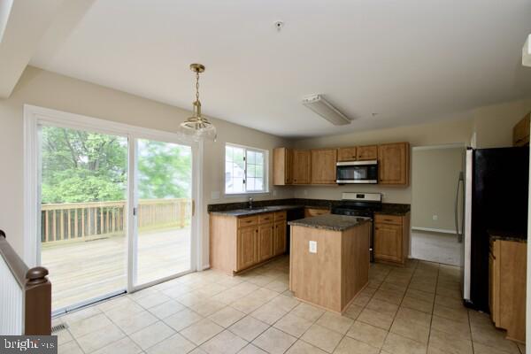 kitchen with stainless steel appliances, dark countertops, a center island, light tile patterned floors, and decorative light fixtures