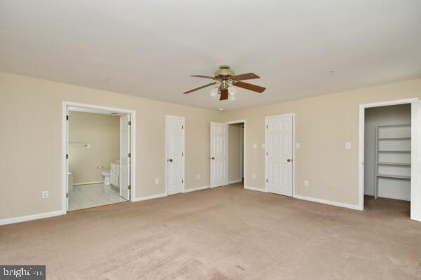 unfurnished bedroom featuring carpet flooring, baseboards, ensuite bath, and ceiling fan