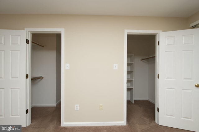 unfurnished bedroom with a walk in closet, a closet, carpet, and baseboards