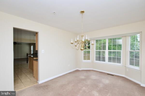 unfurnished dining area featuring a chandelier, baseboards, and carpet floors