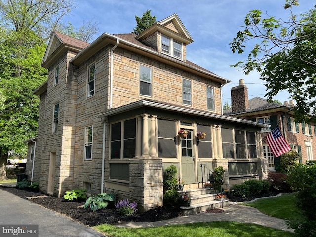 view of front of property featuring stone siding, entry steps, and a sunroom