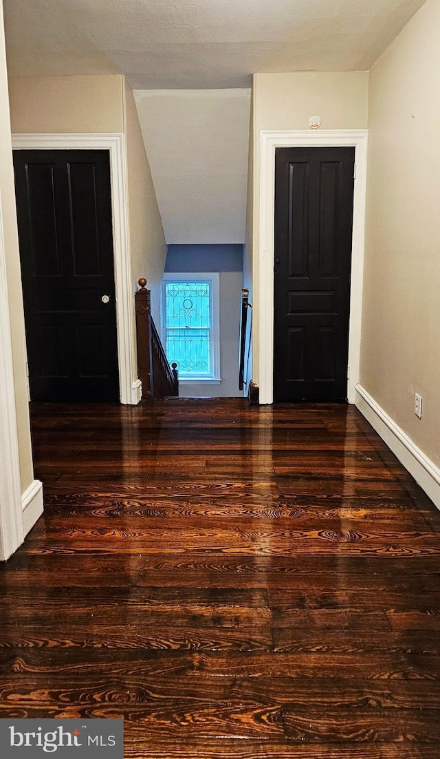 hall with wood finished floors, baseboards, and an upstairs landing