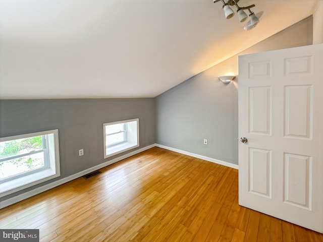 additional living space featuring vaulted ceiling, plenty of natural light, light wood-type flooring, and baseboards