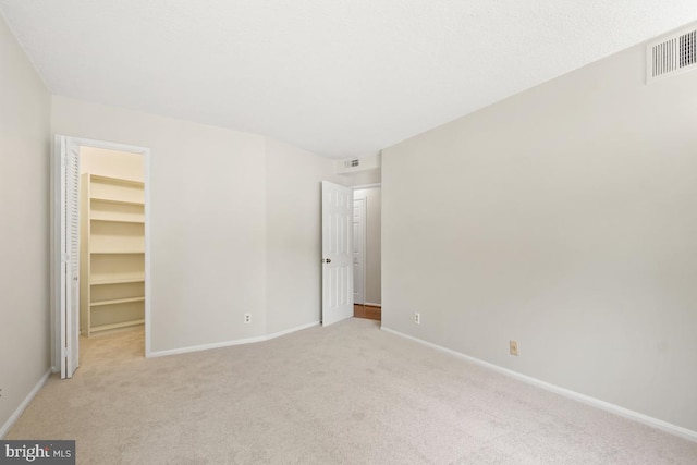 unfurnished bedroom featuring a walk in closet, light carpet, baseboards, and a closet