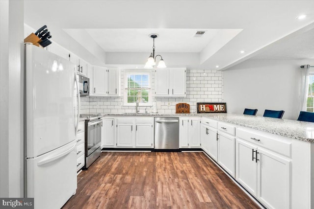 kitchen featuring appliances with stainless steel finishes, a peninsula, a sink, a chandelier, and white cabinetry
