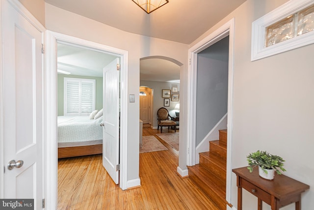 hall featuring arched walkways, light wood-style floors, stairway, and baseboards