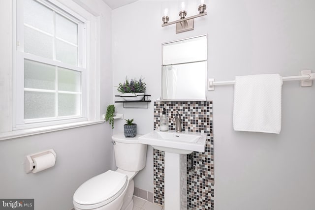 bathroom featuring toilet, tasteful backsplash, tile patterned floors, baseboards, and a sink