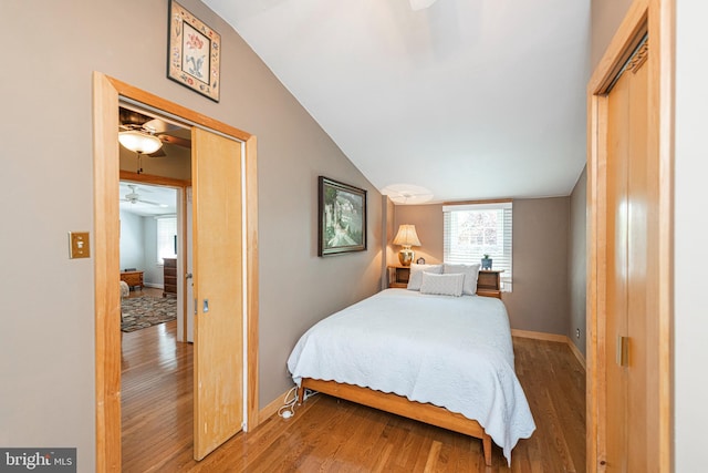 bedroom featuring wood finished floors, multiple windows, baseboards, and vaulted ceiling
