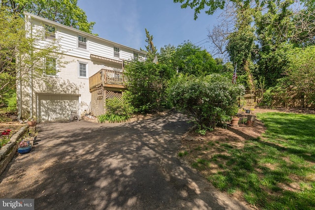 rear view of property with asphalt driveway, a wooden deck, an attached garage, and stucco siding