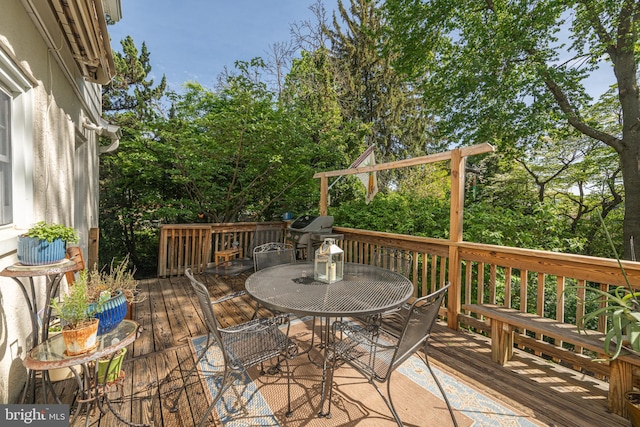 wooden terrace featuring outdoor dining space and view of scattered trees