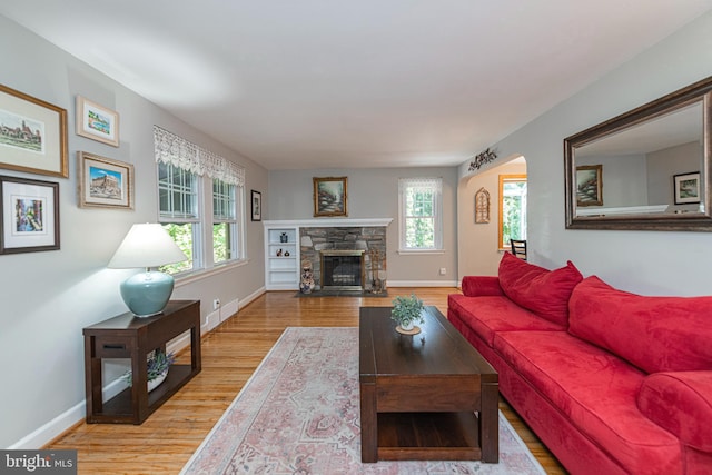 living room with wood finished floors, baseboards, a fireplace, and arched walkways