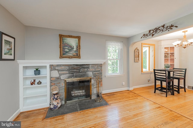 living room with wood finished floors, baseboards, a chandelier, and a stone fireplace