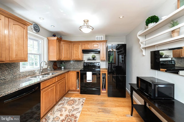 kitchen with black appliances, a sink, under cabinet range hood, light stone countertops, and backsplash