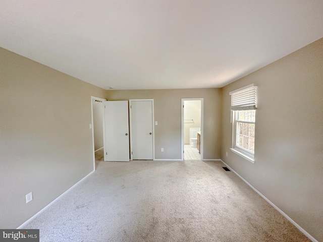 unfurnished bedroom with light colored carpet, baseboards, and ensuite bathroom